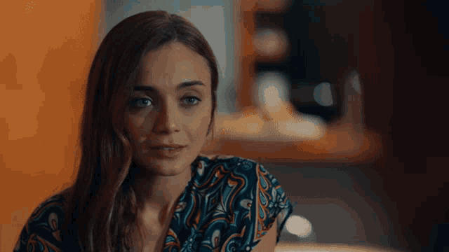 a woman in a colorful shirt looks at the camera with a serious look on her face