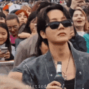 a man wearing sunglasses is standing in a crowd holding a bottle of beer .