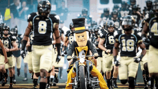 a group of football players are walking on the field with a mascot wearing a top hat