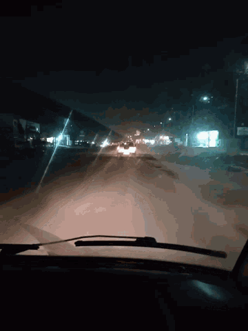 a car windshield with a wiper on it shows a dark street at night