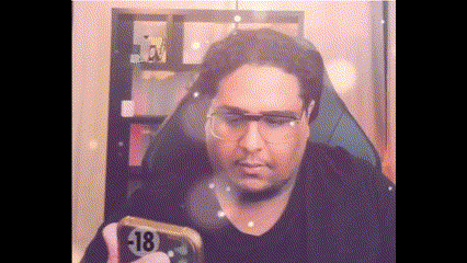 a man wearing glasses is sitting in a chair holding a cell phone with a sticker that says 18 on it .