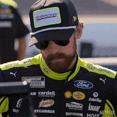 a man with a beard wearing a hat and sunglasses is looking down .