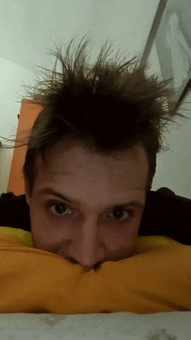 a young man with messy hair is laying on a yellow pillow