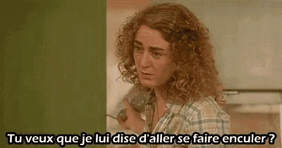 a woman with curly hair is talking on a phone in a kitchen .