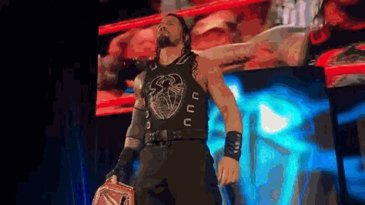 roman reigns is standing on a stage holding a wrestling championship belt