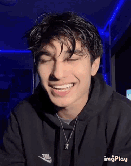 a young man in a black nike hoodie is making a funny face with his tongue out .