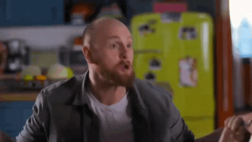 a bald man with a beard is making a funny face in a kitchen .