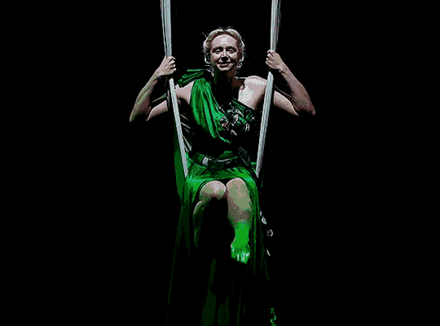 a woman in a green dress is sitting on a swing in the dark