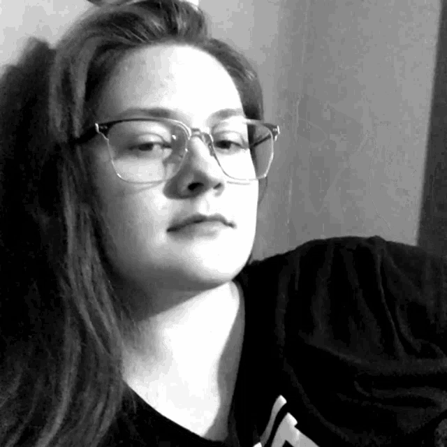 a black and white photo of a woman wearing glasses and a black shirt with the letter t on it