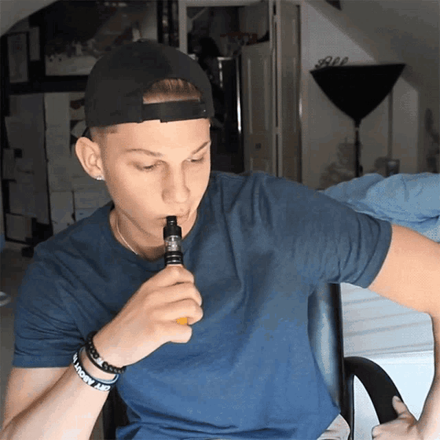 a man wearing a black hat and a blue shirt is smoking an electronic device