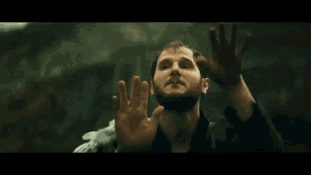 a man with a beard is smoking a cigarette and covering his face with his hands in a dark room .