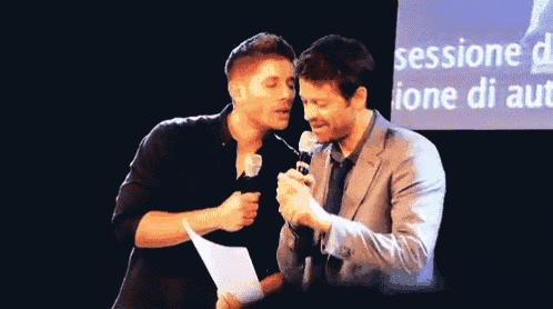 two men are speaking into microphones in front of a sign that says sessione
