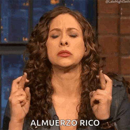 a woman with curly hair is holding her fingers crossed and says almuerzo rico .