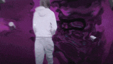 a person in a white hoodie is standing in front of a purple wall