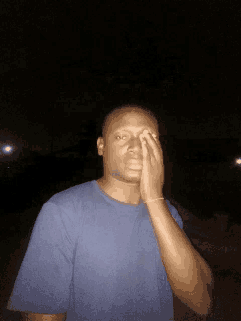 a man in a blue shirt covering his face with his hand