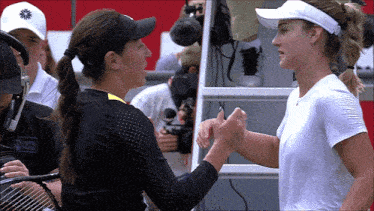 two female tennis players shaking hands with one wearing a white shirt that says ' swiss army ' on it