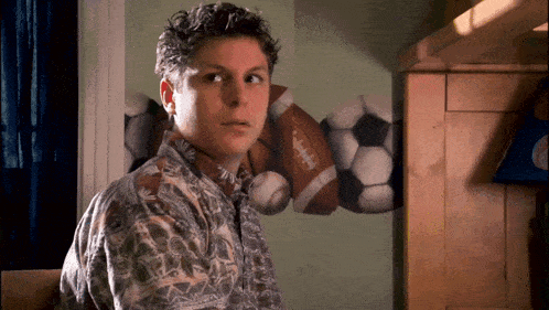 a young man stands in front of a wall with a picture of footballs and soccer balls