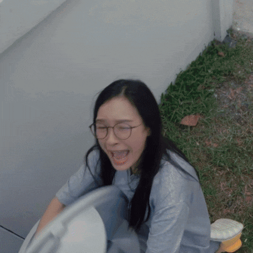 a woman wearing glasses sits on a toilet and laughs