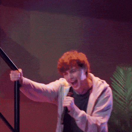 a man is singing into a microphone while standing on a set of stairs