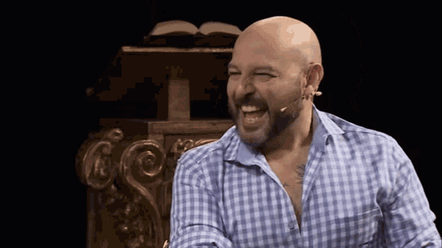 a bald man with a beard wearing a blue and white plaid shirt is laughing