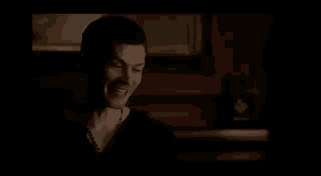 a man is laughing in a dark room while holding his hands to his face .