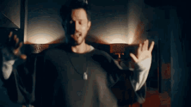 a man with a beard is standing in a dark room with his arms outstretched and singing .