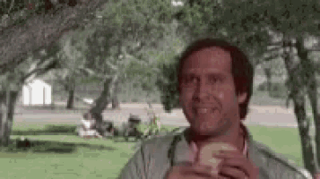 a man is sitting in a park eating a sandwich and smiling .
