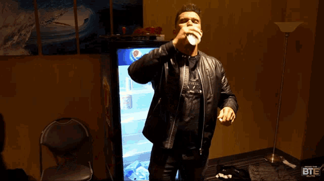 a man in a leather jacket holds a bottle of water in front of a vending machine that says bte