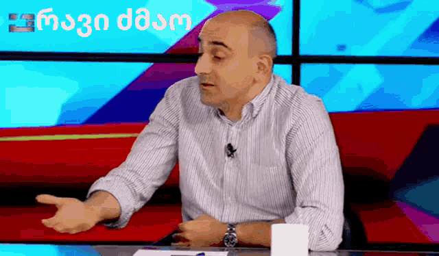a man in a striped shirt is sitting at a table with a cup of coffee and a microphone