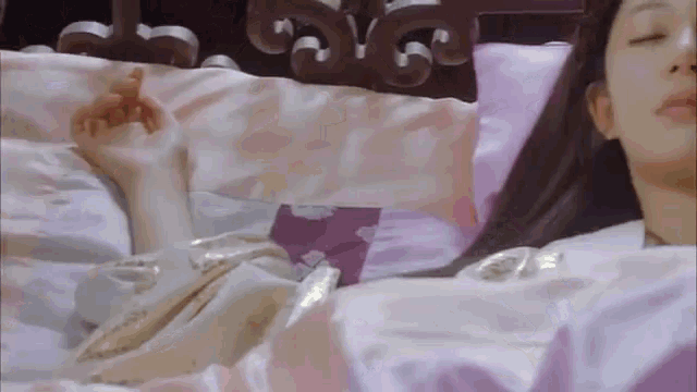 a woman is laying on a bed with her eyes closed and a purple pillow .