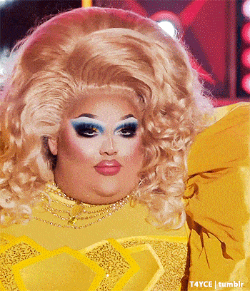 a drag queen is wearing a yellow dress and has a big blonde wig
