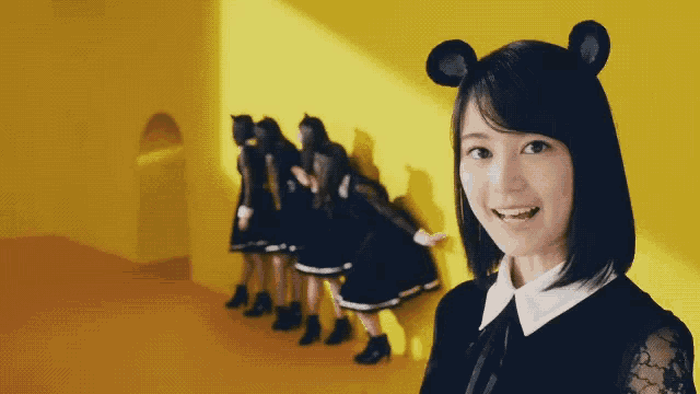 a girl wearing a mouse ear headband is smiling in front of a yellow wall