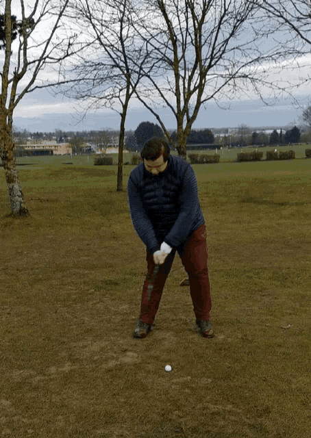 a man in a blue jacket is swinging a golf club at a golf ball