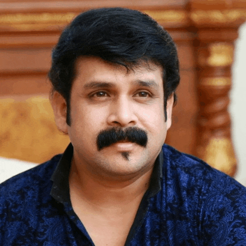 a man with a mustache and a blue shirt is looking at the camera