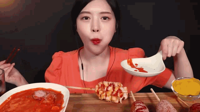 a woman in an orange shirt is eating food with chopsticks and a spoon