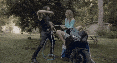 a woman sits on a motorcycle while a man sprays water on her