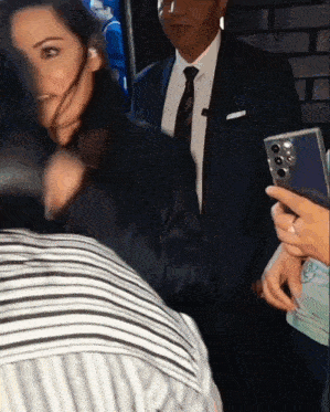 a man in a suit and tie is standing next to a woman holding a cell phone