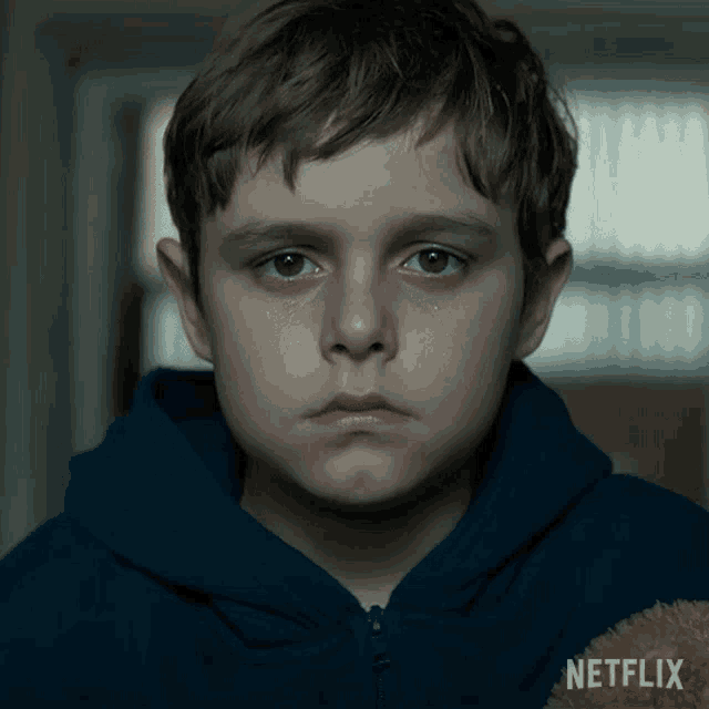 a boy with tears running down his face is holding a teddy bear and a netflix logo is visible in the corner