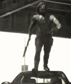 a man in a superhero costume is holding a gun while standing on top of a car .