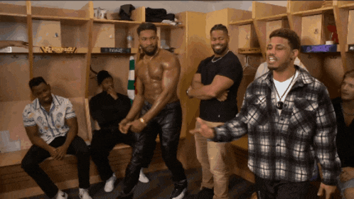 a group of men are standing in a locker room and one of them is wearing a shirtless shirt