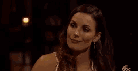 a woman is smiling and looking at the camera while sitting at a table in a dark room .