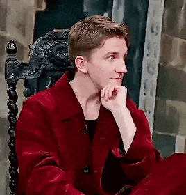 a man in a red coat is sitting in a chair with his hands on his chin .