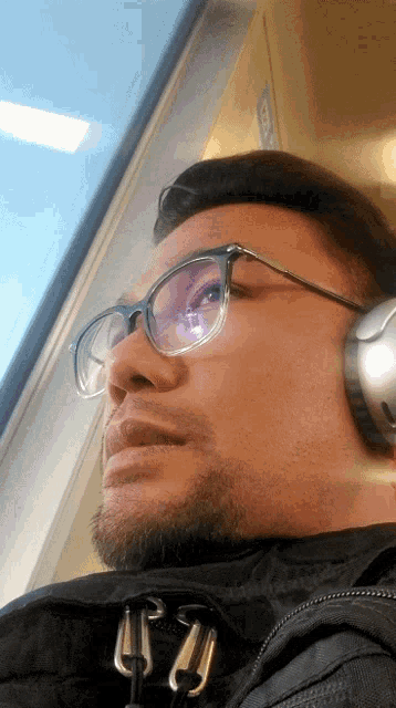 a man wearing glasses and headphones looking out a window
