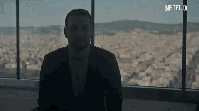 a man in a suit is sitting in front of a window with netflix written on the bottom