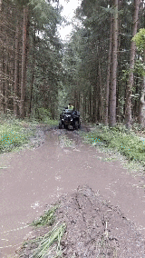 a black atv is driving down a muddy road in the woods