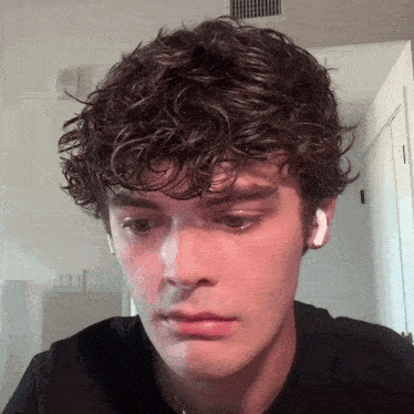 a young man with curly hair is wearing a black shirt