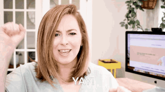 a woman says yay in front of a computer screen