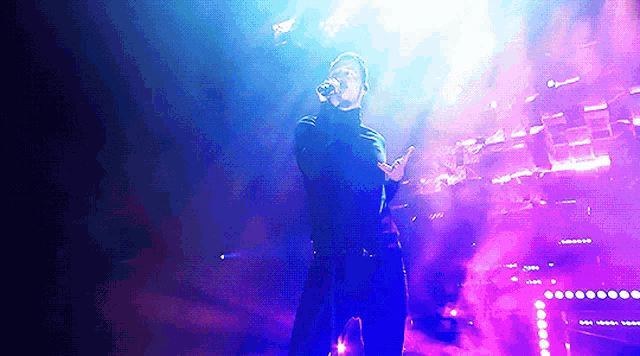 a man is singing into a microphone on a stage with purple lights