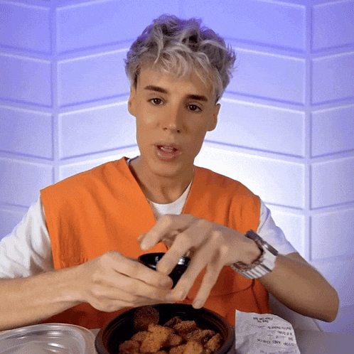 a man wearing an orange vest is eating chicken nuggets