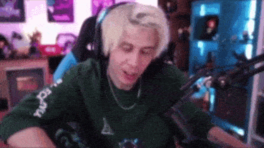 a man with blonde hair is sitting in front of a microphone wearing headphones and a green sweater .